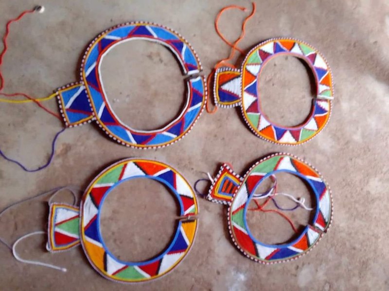 Overhead view of unfinished beaded collars and rings laid on the ground, geometric colour patterns