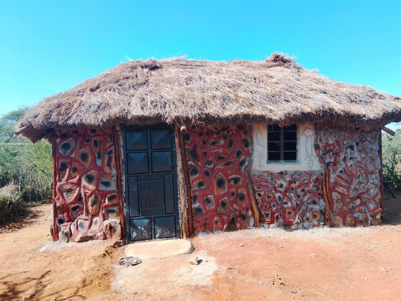 Hand-painted thatched hut with red-ochre and white geometric patterns, inside the Naisuyo manyatta