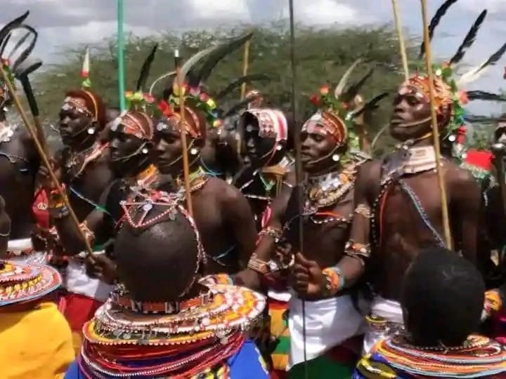 Maasai men in feathered ceremonial headdresses and beadwork, spears in hand, at a community gathering