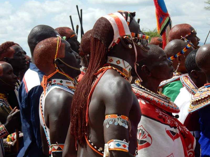 Close side-profile of Maasai warriors with ochre-dyed hair and beaded armbands at a ceremony